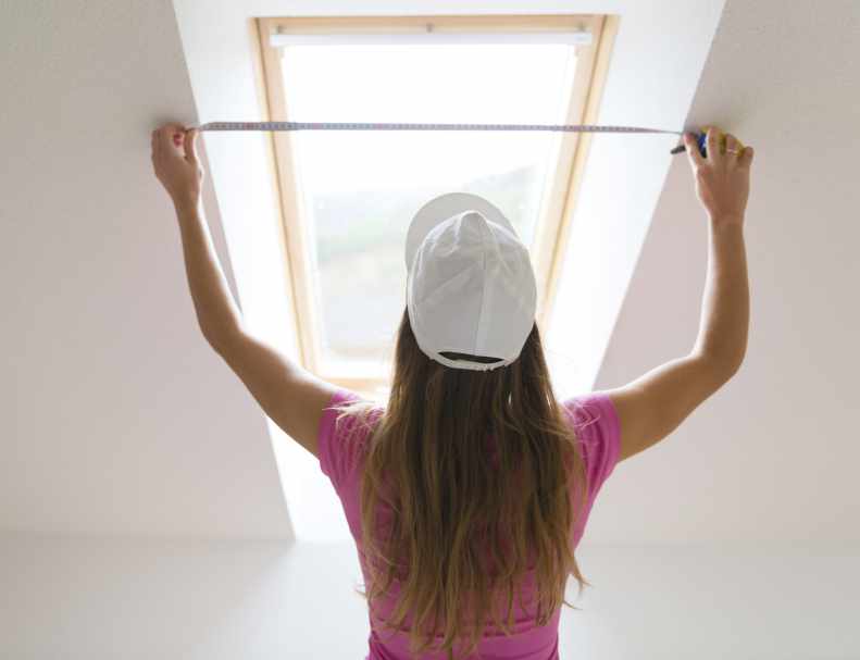 Rear view of young woman measuring the wall with tape measure